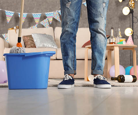Man cleaning up after a party with a bucket and mop.